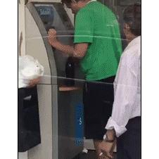A drunk guy with a beer tries to use an ATM.