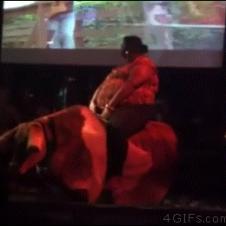 A rotund woman rolls off of a mechanical bull.