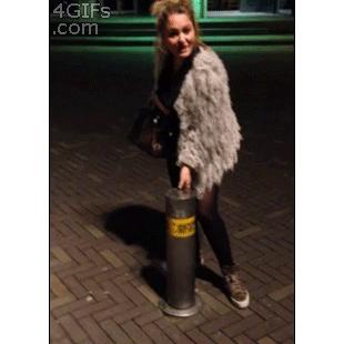 A girl sits on top of a bollard.
