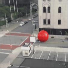 A giant red ball rolls along the street.