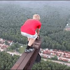 A kid stands on a ledge of a very high tower for the thrill of it
